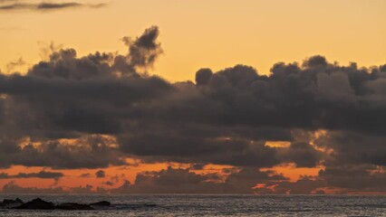 Orange and yellow sky as the sunsets between clouds over the ocean - timelapse