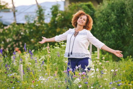 Outdoor portrait of beautiful 50 year old woman enjoying nice day in flower park or garden, happy and healthy lifestyle