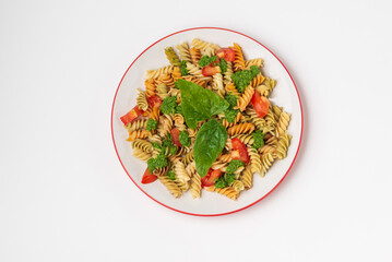 Spiral colored fusilli pasta with with green spinach sauce and tomatoes on plate isolated on white, top view