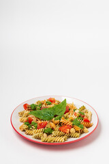 Spiral colored fusilli pasta with with green spinach sauce and tomatoes on plate isolated on white with copy space