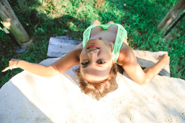 A girl lounges at a table sitting and leaning on a concrete white tabletop. A gazebo with a bench and table and a girl in it, dressed in a top and jean shorts 