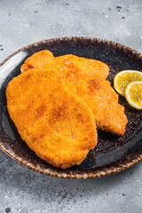 Roasted breaded german weiner schnitzel on a plate. Gray background. Top view - obrazy, fototapety, plakaty