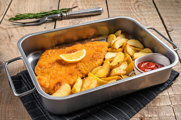 Pork meat weiner schnitzel with potato wedges and tomato sauce in steel tray. Wooden background. Top view - obrazy, fototapety, plakaty