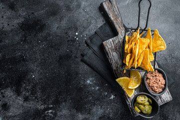 Mexican nachos corn chips with Chili con carne and jalapeno in a basket. Black background. Top view. Copy space