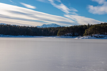 Scenic view of frozen alpine lake Forstsee, Techelsberg, Carinthia (Kaernten), Austria, Europe. Breathing fresh cold air. Winter wonderland at morn. Snow capped Karawanks mountain range behind forest