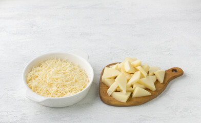 A white bowl with grated cheese and a wooden board with sliced cheese on a light gray background. Cooking homemade vegetarian food