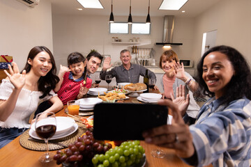 Authentic shot of happy carefree smiling woman making selfie or video call to friends or relatives in New Year party with Multi-ethnic family