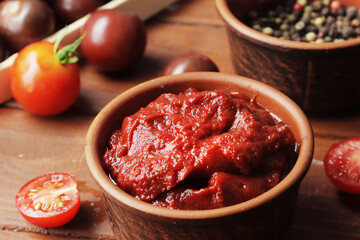 Bowl full of tomato sauce, Wooden spoon full of tomato sauce, spices, seasonings, Sliced ripe cherry tomato slices,  