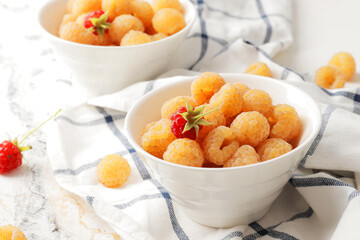 Ripe yellow raspberries in a bowl with a tea towel on a marble background. A bowl full of raspberries. Dessert ingredients.