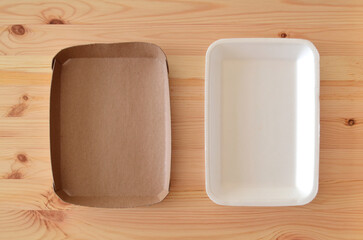 Top view of a recyclable cardboard empty food tray as an environmentally friendly alternative next to a polystyrene container (number 6 plastic), with a wooden background.