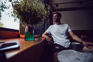 African american man in a white t-shirt sits in a coffee shop and uses the phone. Mock-up.