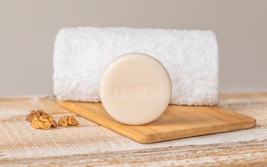 Round shape dry handmade shampoo bar with text 'shampoo',made of cold pressed oil, vegan formula,lays on wooden table,nuts,white towel is behind. Silicones, sulfates,artificial colourants,plastic free