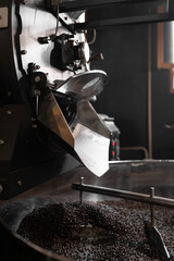 Dark roasted coffee grains being mixed inside of a roaster machine cooling tray