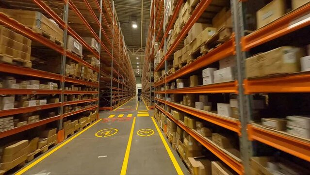Forklift truck racks with boxes and worker pulling trolley in spacious warehouse first point view. Plant products storage