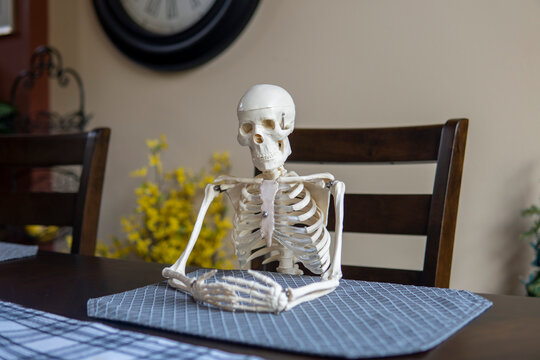 Skeleton sits alone at table in the room. Loneliness concept