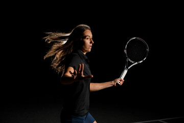 Fototapeta na wymiar Close-up side view portrait of excited woman with brown flowing hair in black tennis uniform with tennis racket