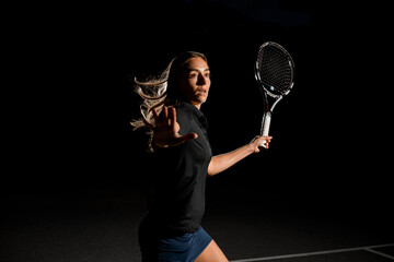 side view of excited woman with brown flowing hair in black tennis uniform with tennis racket