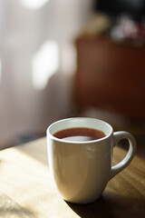 A mug full, coffee, tea set on a wooden table, morning sun and in the background light pink curtains
