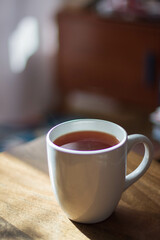 A mug full of coffee or tea set on a wooden table, morning sun and in the background light pink curtains
