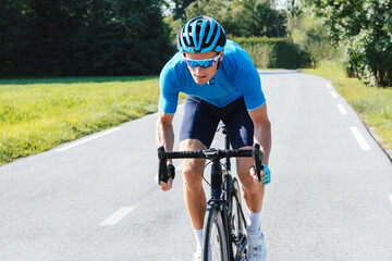 Professional road cycling male racer taking an aerodynamic body position for sprinting on a bike,...