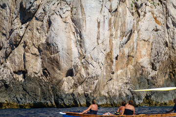 Tourists in small boat viewing Capri cliffs from the Mediterranean Sea
