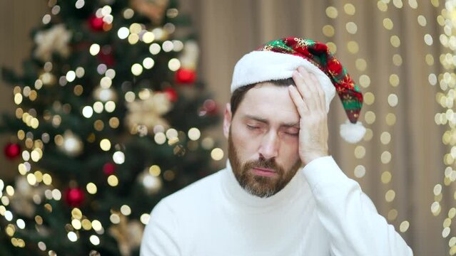 portrait of a man with a headache after celebrating New Year eve holiday party with a hangover. Male with a bad head Nausea and poor health at home on the background of a Christmas tree