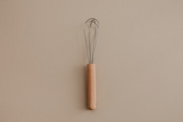 A wooden whisk beater on beige paper background. Flat lay, top view copy space. Natural light, kitchen tool. 