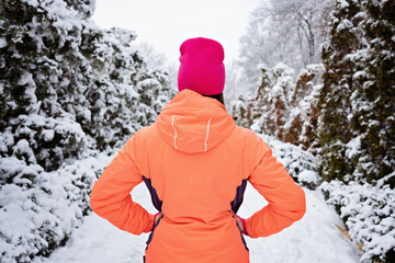 Winter workout, exercising in cold weather. Winter fitness, Safety tips for exercising outdoors. Sporty woman in sportswear standing in winter snowy park, forest.