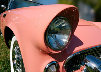 Close-up detail of the front fender and headlamp of a pink 1950s sports car