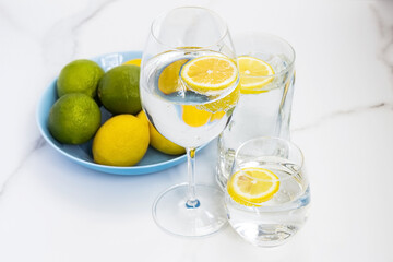 A glass of water, lemon and mint and lime on a white table for healthy life, energy, thermoregulation and normalization of digestion