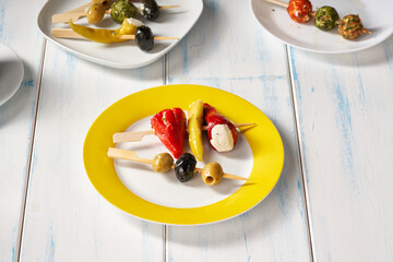 Finger food sticks with olives and stuffed pepperoni on yellow plate.