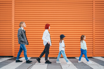 Fashion-dressed quartet of small kids and teenager sisters and brothers crossing a pedestrian zebra...