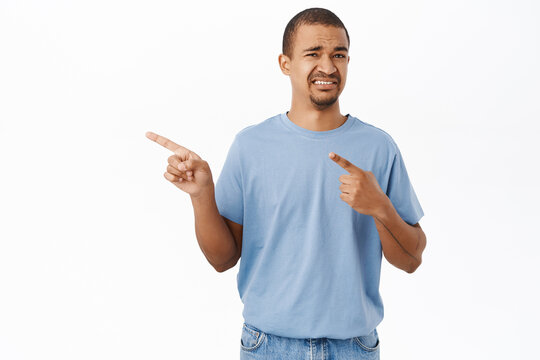 Phew Cringe. Disgusted Guy Pointing Fingers Left, Grimacing And Looking Displeased, Standing Over White Background