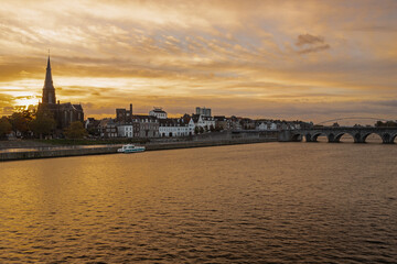 Obraz premium Maastricht, Netherlands 10-24-2022 Skyline of the Wyck area in downtown Maastricht with views on the iconic Servaas bridge and brewery. With a sunrise in Autumn coloring the sky in dramatic cloudscape