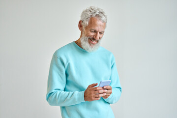 Older happy senior bearded stylish hipster man holding cell phone looking at cellphone using smartphone checking mobile apps news or communicating online standing isolated on white wall.
