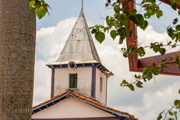 A torre da igreja vista entre o tronco de um coqueiro e folhas de uma trepadeira. O Santuário Nossa Senhora Aparecida fica na cidade de Aparecida de Goiânia.