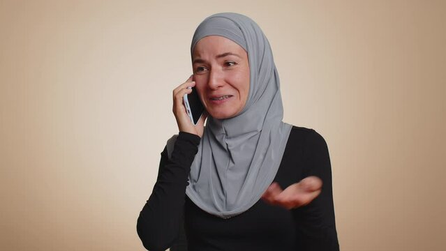 Happy young muslim woman in hijab making call using mobile cell phone, talking pleasant conversation with good friend or family. Arabian female girl speaking on smartphone on studio beige background