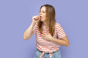 Portrait of sick unhealthy blond woman wearing striped T-shirt having cough and feeling pain in her lungs, catching cold, flu symptoms. Indoor studio shot isolated on purple background.