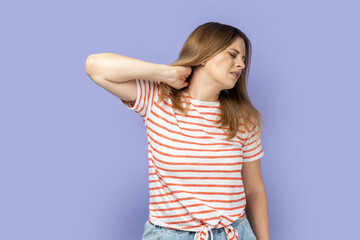 Portrait of attractive tired upset unhealthy blond woman wearing striped T-shirt standing massaging...