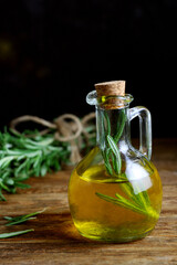 Olive oil with rosemary stands on a wooden table. Next to it is rosemary. dark moody. selective focus