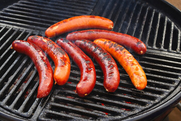 Traditionelle deutsche Bratwurst vom Grill angeboten als close-up auf einem Holzkohlegrill mit Feuer und Rauch 