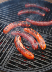 Traditionelle deutsche Bratwurst vom Grill angeboten als close-up auf einem Holzkohlegrill mit Feuer und Rauch 