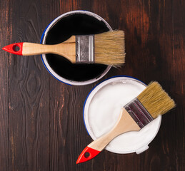 Open can with white and black paint and brushes on wooden background, top view