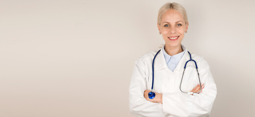 Young blonde doctor standing against gray background smiling at camera.Copy space banner.Place for text