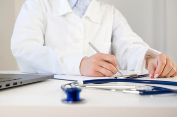 Doctor in a white labcoat writing out prescription or filling the form in the cabinet at hospital.Healthcare concept