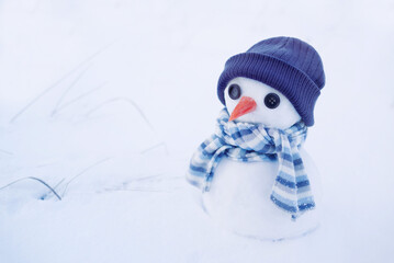 Little cute snowman made of snow globes in a knitted hat and scarf on the snow on a winter day close-up, soft selective focus. Festive Christmas background, symbol of winter