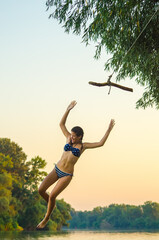 Teenage girl jumping into the river from swinging rope in summer