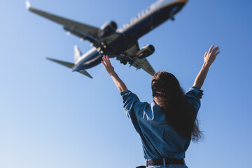 Girl and airplane in flight, landscape with woman standing with hands raised up, waving arms and flying passenger airplane, female tourist and landing commercial aircraft, summer sunny day