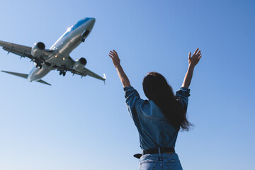 Girl and airplane in flight, landscape with woman standing with hands raised up, waving arms and flying passenger airplane, female tourist and landing commercial aircraft, summer sunny day