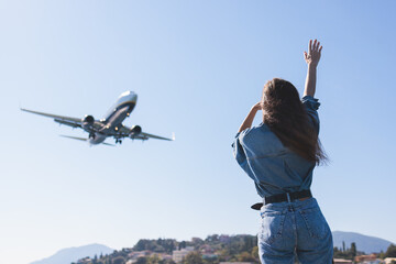 Girl and airplane in flight, landscape with woman standing with hands raised up, waving arms and flying passenger airplane, female tourist and landing commercial aircraft, summer sunny day